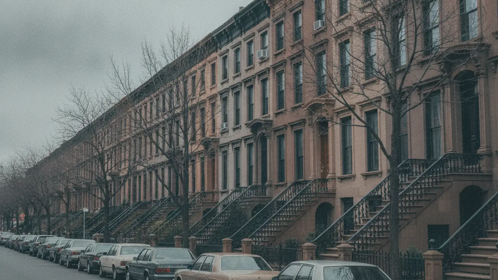 A Brooklyn brownstone block with a continuous row of stoops and cornices under bare street trees.