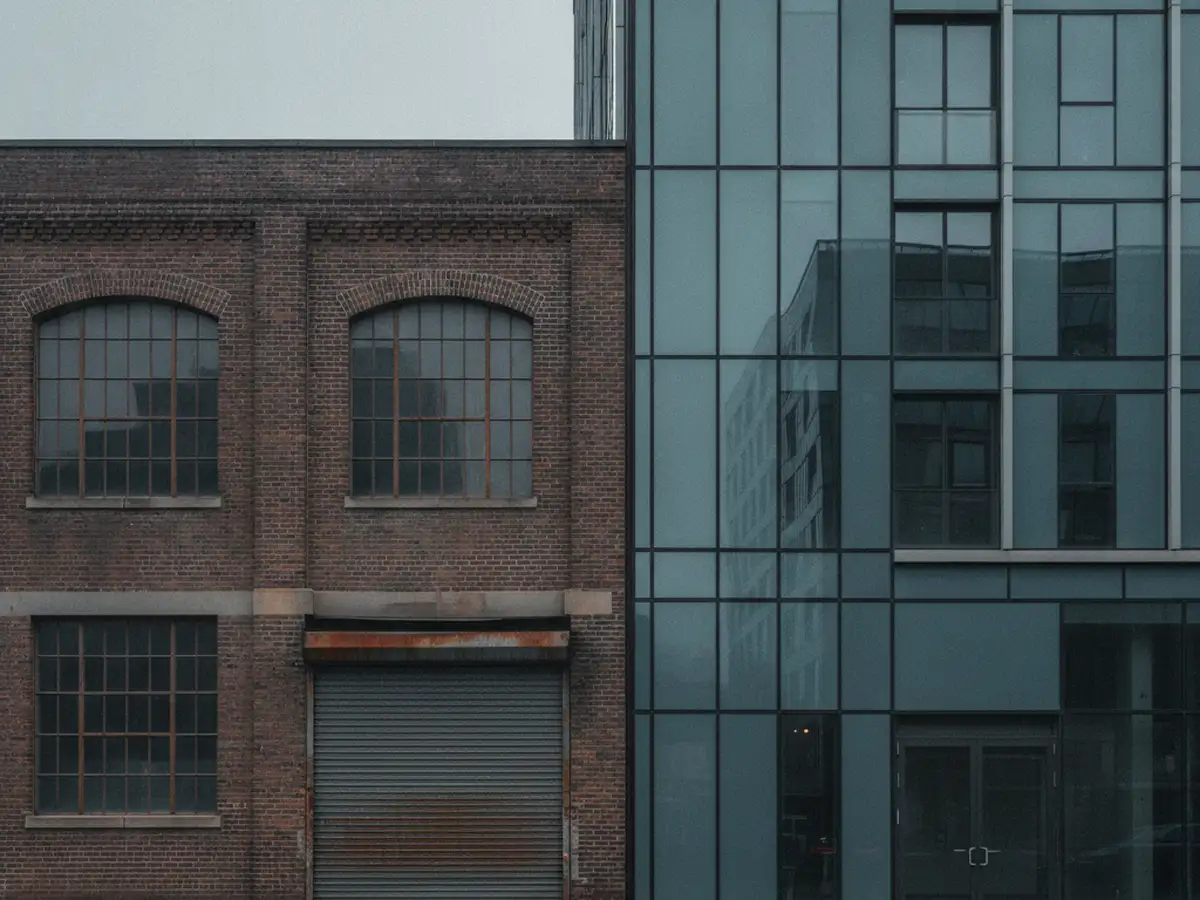 A north Brooklyn street where a converted brick warehouse stands beside a new glass apartment tower.