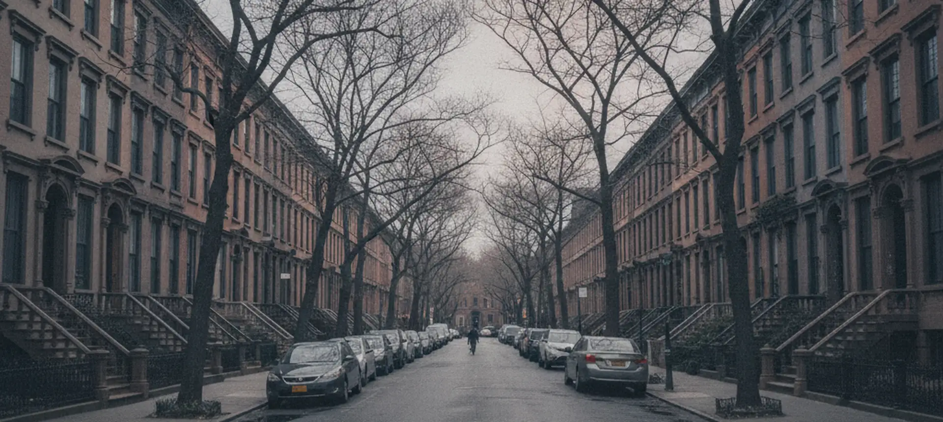 A long Brooklyn brownstone street in deep perspective, stoops on both sides and bare trees meeting overhead.